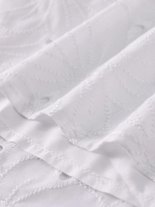 Detail of white Broderie Anglaise fabric showing intricate floral embroidery and eyelets
