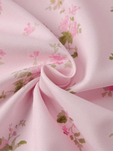Detail shot of soft pink floral chiffon fabric with delicate roses and green leaves