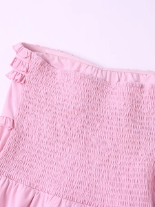 Detailed view of pink smocked dress with ruffle trim and elastic pleated texture