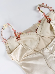 Détail de robe en satin champagne avec broderie florale sur bretelles et fermeture éclair