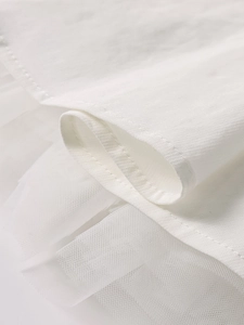 Detail of white dress showing layered woven fabric and delicate mesh hem stitching