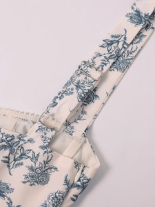 Detail of blue floral dress featuring adjustable straps, metal buckles, and white lace trim