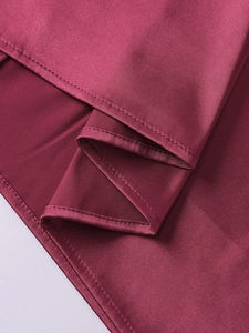 Détail de l'ourlet d'une robe en satin bordeaux avec coutures et texture soyeuse