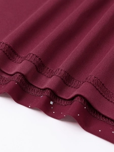 Détail macro du tissu en maille bordeaux avec paillettes argentées et couture de l'ourlet