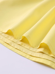 Detail of yellow pleated dress hem featuring precise double-needle stitching and fabric texture
