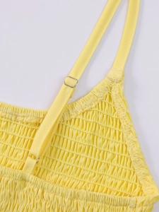 Detail of yellow smocked fabric with adjustable spaghetti straps and silver metal buckles