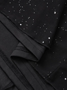 Dettaglio macro del tessuto a rete nero con paillettes argentate e cuciture fini sul vestito