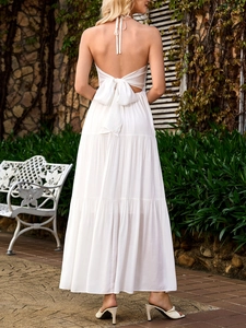 Detail view of white backless maxi dress featuring a large decorative bow and tiered skirt