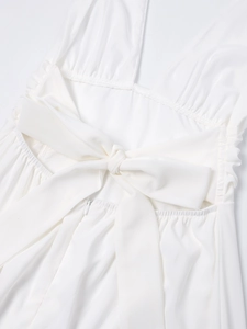 Detail eines weißen Neckholder-Kleids mit großer Rückenschleife, Plissee und Reißverschluss
