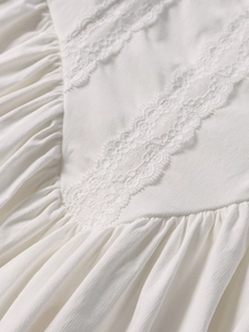 Close-up of white dress showing elegant lace stitching and pleated textured fabric