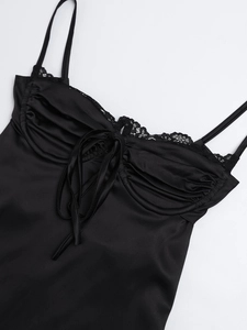Dettaglio di abito in raso nero con pizzo delicato, fiocco e design plissettato sul seno