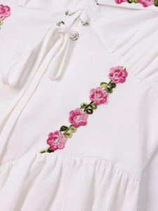 Detail of white dress with floral embroidery, silver eyelets, and adjustable lace-up ties