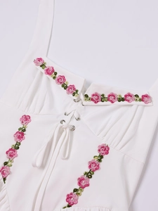 Close-up of white dress with floral embroidery, halter straps and lace-up chest detail