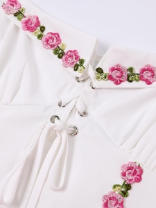 Close-up of halter neck lace-up with silver eyelets and floral embroidery on white dress