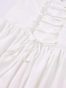 Detail of the white dress featuring a criss-cross lace-up back and fine pleated texture