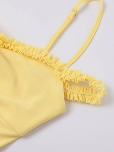 Detail of pale yellow mesh dress with thin straps and delicate ruffle trim neckline