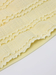 Close-up of light yellow dress with textured pleated fabric and layered lace detail