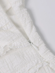 Detail view of white textured halter dress featuring a seamless invisible zipper and pleats