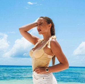 Detail of beige boned corset top with bow straps on a woman against a beach backdrop