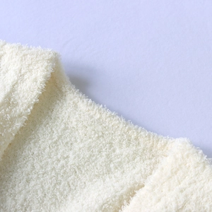 Close-up of soft creamy white plush fabric texture and hem detail of a long fleece cardigan