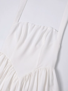 Close-up of white halter dress with V-shaped waist seam and pleated skirt details