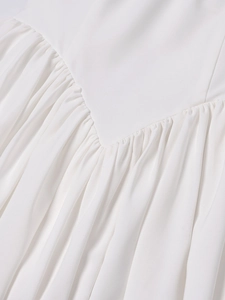 Detailed view of the V-shaped waist seam and delicate gathering on a white dress fabric