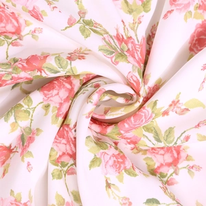 Close-up of soft white floral fabric with elegant pink rose prints and delicate leaf patterns