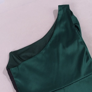 Détail d'une robe en satin vert émeraude avec épaule asymétrique et paillettes noires