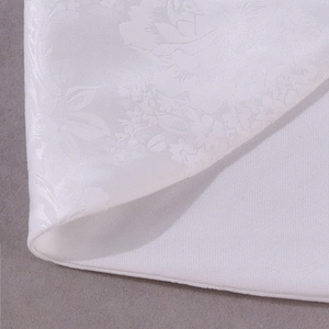 Dettaglio macro del tessuto jacquard bianco con motivi floreali a rilievo e caduta elegante
