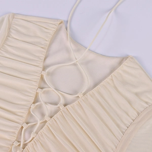 Dettaglio dell'abito a maniche lunghe in mesh con pieghe beige e lacci intrecciati