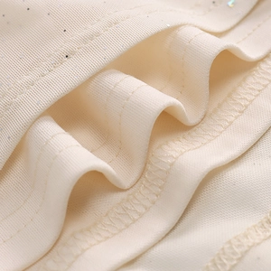 Macro view of cream knit fabric with fine sequins and layered ruffle detail