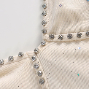 Détail du tissu texturé crème avec reflets colorés et bordure en strass sur la robe