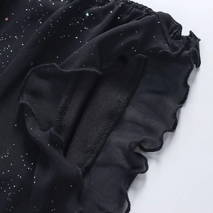 Dettaglio macro del tessuto a rete nero con paillettes brillanti e bordo a balze
