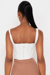 Back view of white corset-style crop top featuring zipper closure and boning detail