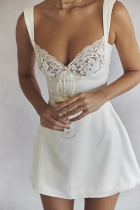 Detail of white satin mini dress featuring delicate lace trim and a small bow on the neckline