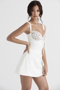 Close-up of white mini dress featuring floral lace patchwork and delicate bow detailing