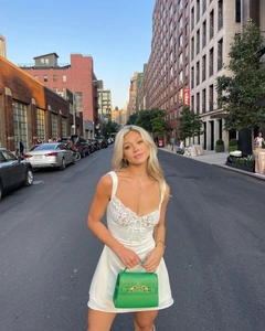 Detail of white satin dress with lace trim and corset ties paired with a green bag