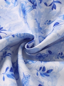 Makro-Detail von blauem Blumendruck auf weißem Stoff mit weichem Faltenwurf
