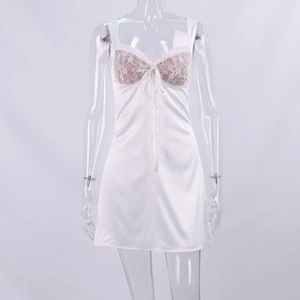 Close-up of white satin slip dress featuring floral lace patchwork and a small ribbon bow