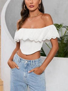 Dettaglio del crop top bianco con spalle scoperte, ricamo a occhielli e volant