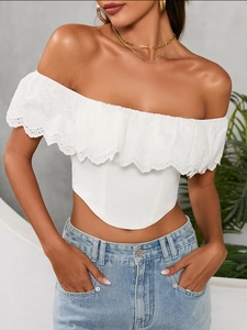 Dettaglio del crop top bianco con spalle scoperte, ricamo a occhielli e bordo a balze