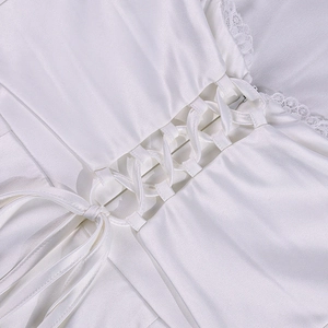 Detailed close-up of white satin dress featuring cross-strap lacing and lace trim