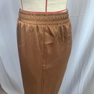 Close-up of brown satin wide-leg trousers showing elastic high waist and silky fabric