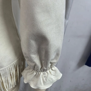 Macro view of cream faux suede fabric showing fringe tassels and ruffled sleeve cuffs