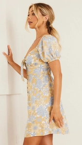 Détail de robe courte fleurie avec manches bouffantes et fermeture nouée à l'avant