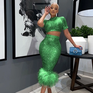 Dettaglio del crop top di paillettes verde smeraldo e gonna midi con piume sul fondo