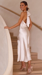 Robe midi élégante en satin champagne avec licou et nœud au dos sur un escalier
