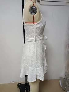 Detail of white floral lace mini dress featuring a self-tie belt and ruffled hemline