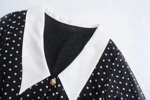 Close-up of white contrast collar with golden button on black polka dot chiffon dress