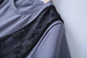 Detail shot of grey-blue fabric with delicate black lace floral embroidery and trim
